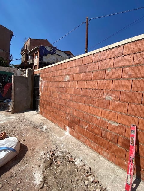 Red brick wall under construction in an urban residential area with buildings and power lines visible under clear blue sky