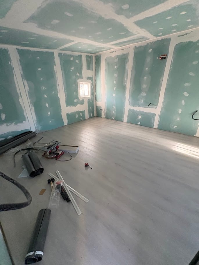 Interior room under renovation with drywall and tape on walls and ceiling, construction tools on white floor