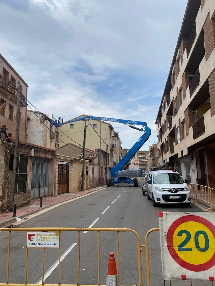 Urban street with blue articulated lift truck, white service vehicle, barricades, and 20 km/h speed limit sign