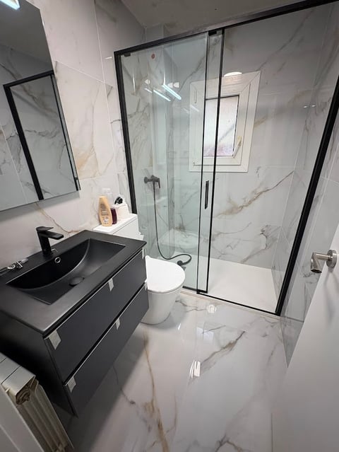 Modern bathroom with black vanity, vessel sink, marble-look flooring and shower enclosure with black frames and glass doors