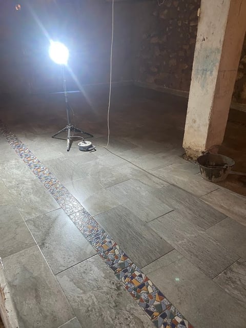 Construction site interior with bright work light on tripod, concrete floor with decorative stripe, and weathered column